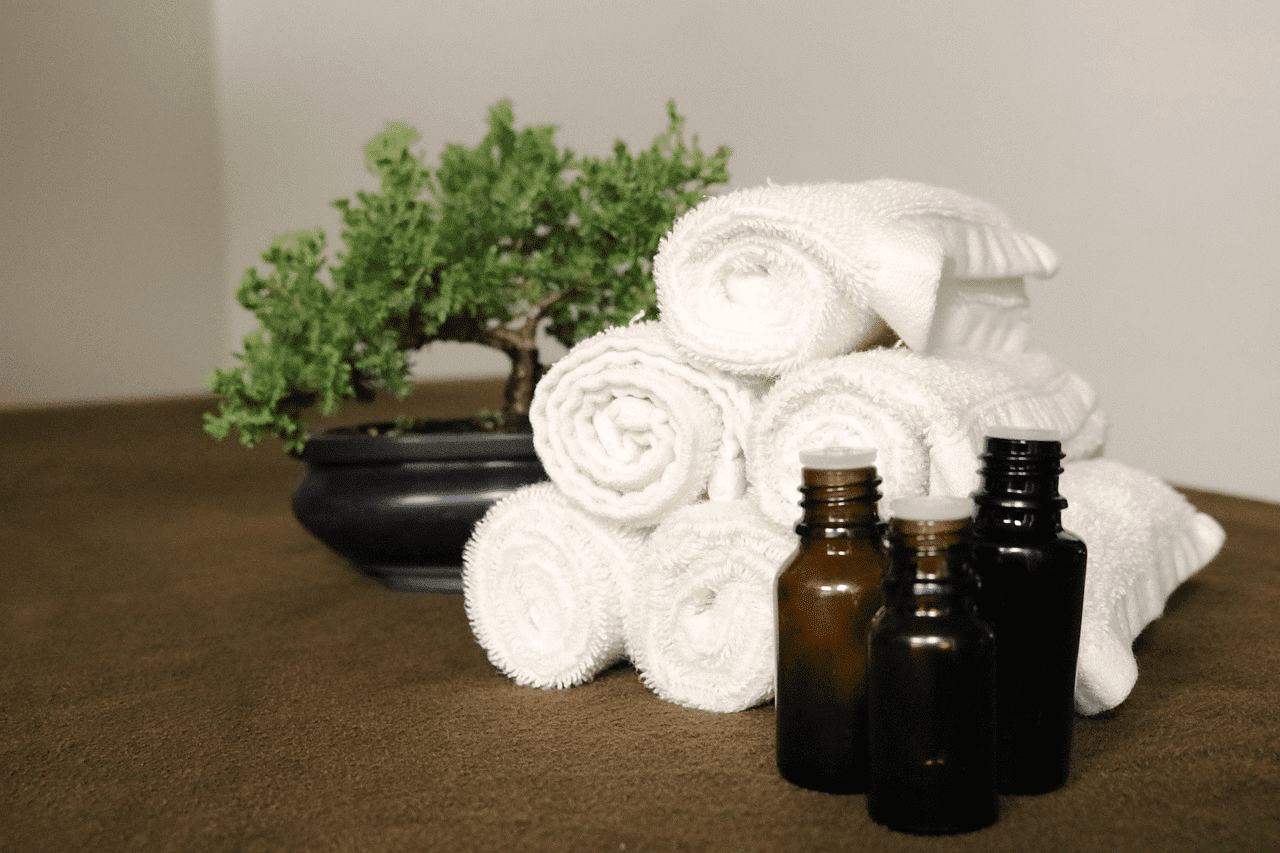 Rolled white towels, essential oil bottles, and small bonsai tree on a table.