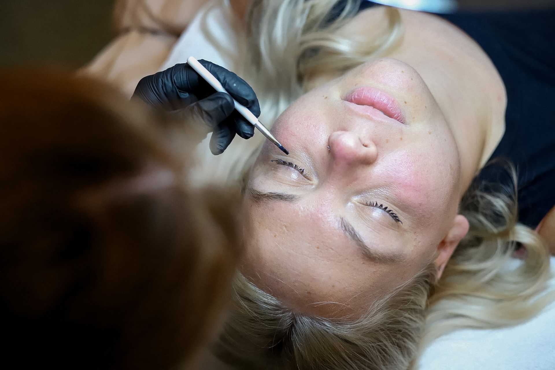 Woman receiving eyebrow microblading treatment in a salon.