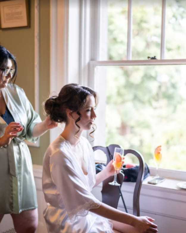 Bride getting ready near window with champagne.