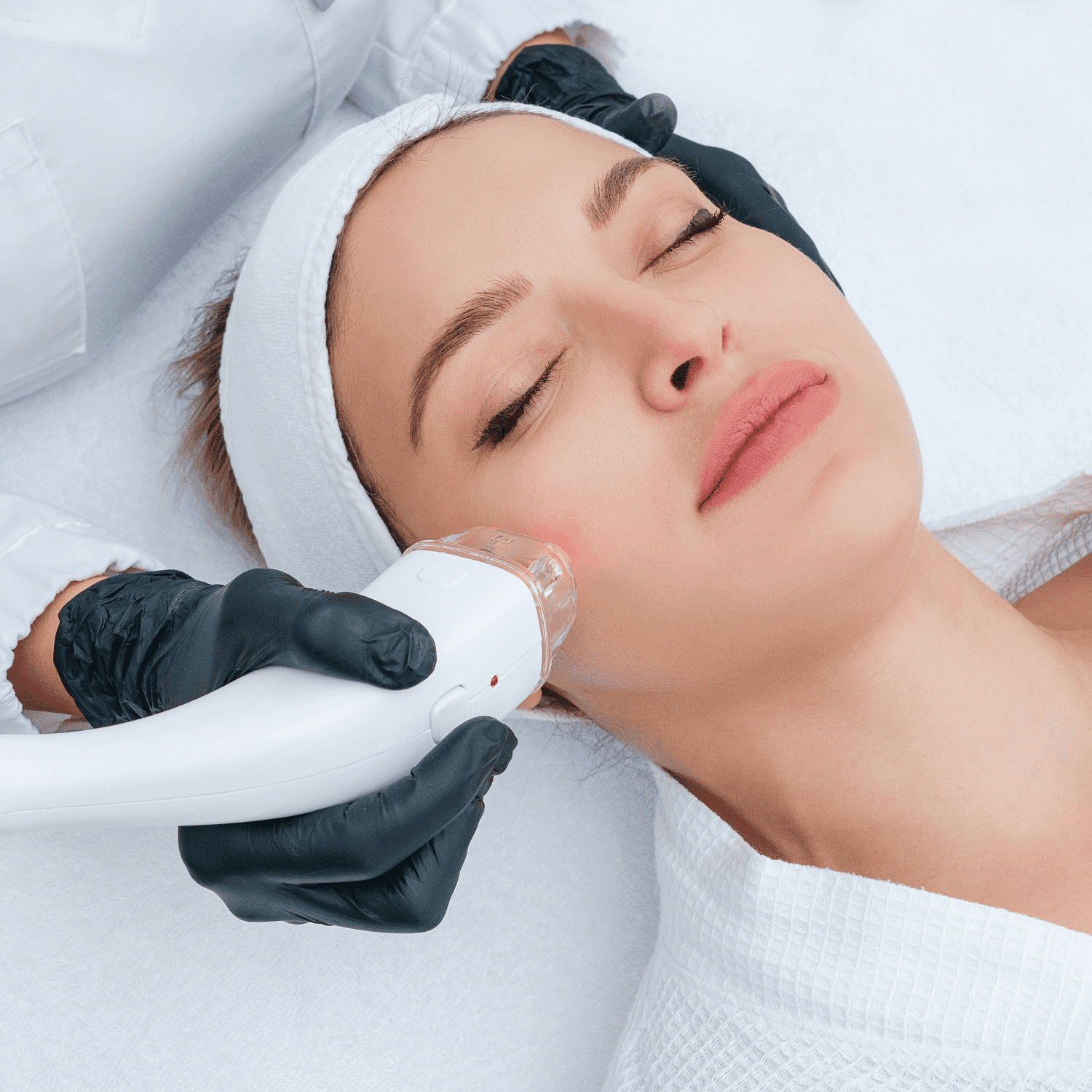 Facial treatment with a handheld device, woman relaxed, aesthetician wearing gloves.