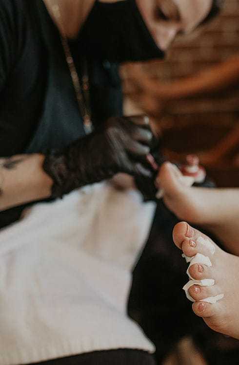 Person receiving a pedicure with black-gloved technician applying nail polish.