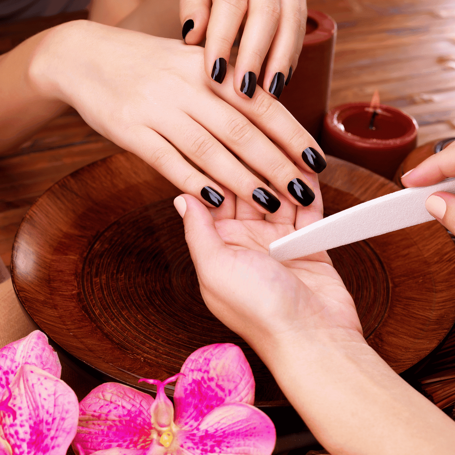 Manicure session with black nail polish, wood bowl, flowers, and candles.