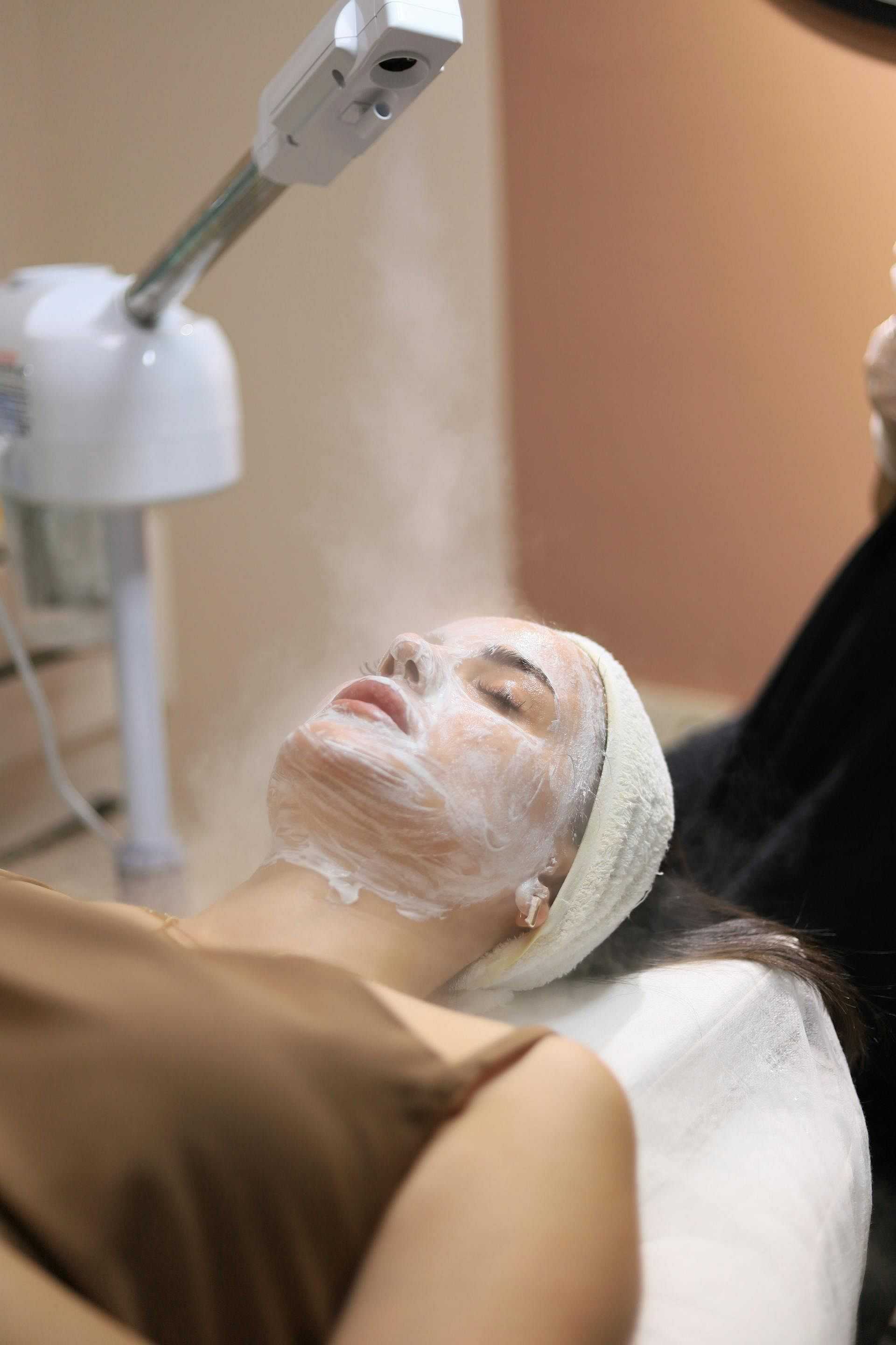 Facial spa treatment with steam and face mask on a relaxed person in a spa setting.