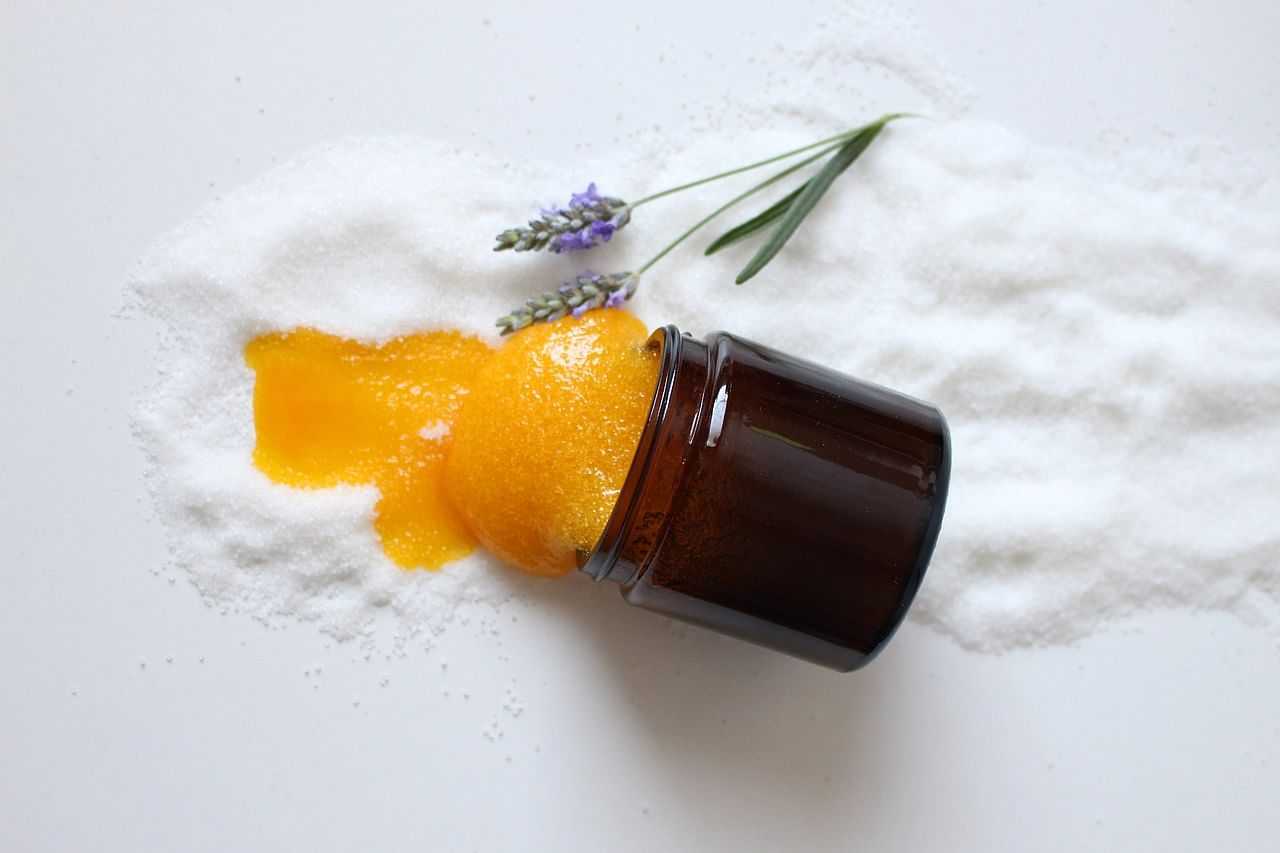 Jar of orange scrub spilled on salt with lavender sprigs nearby.
