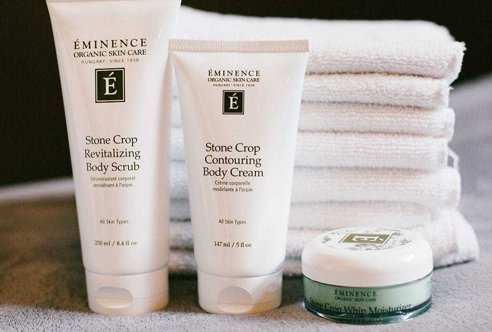 Éminence skin care products with towels, including body scrub, contour cream, and moisturizer.