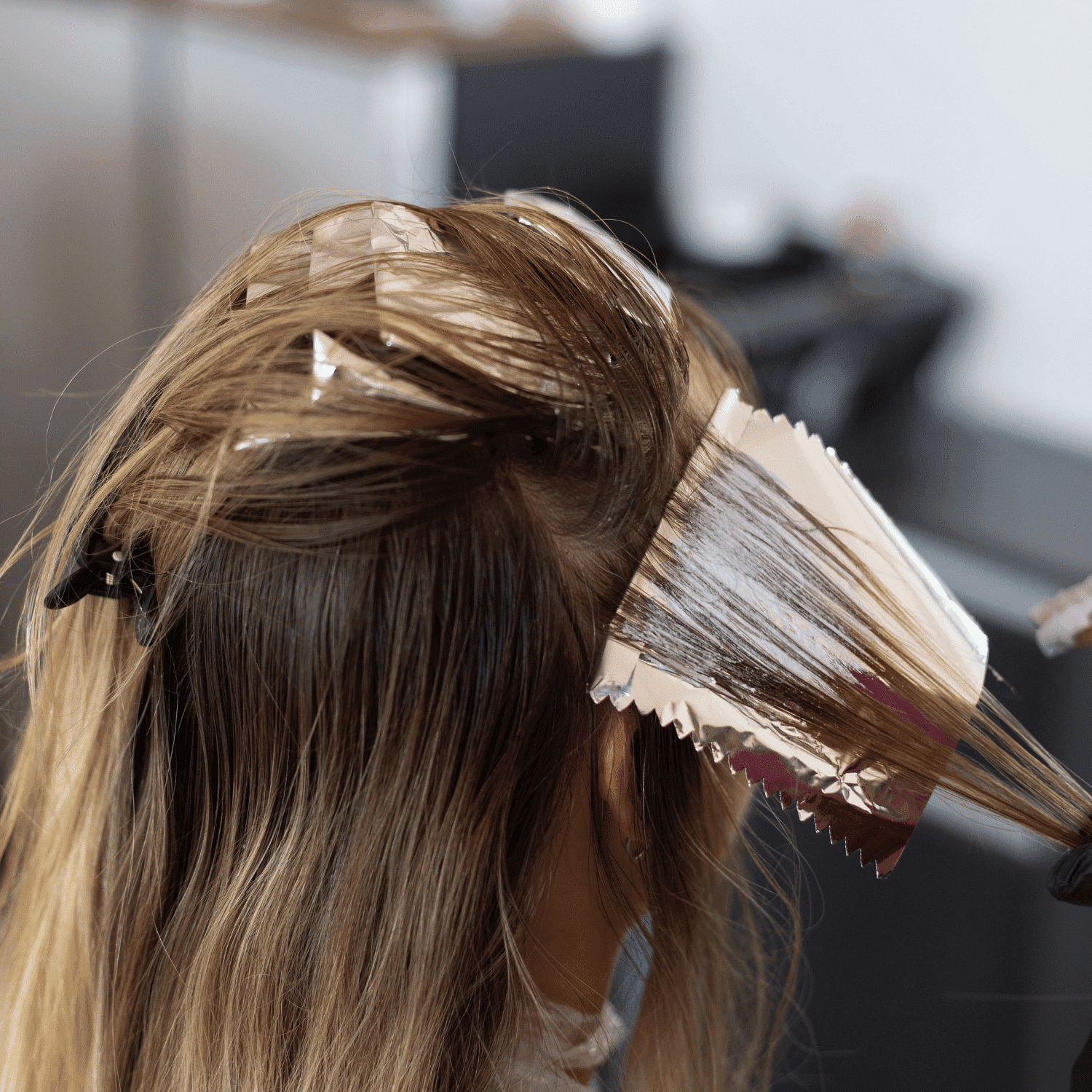 Hair coloring in progress, with foil sheets separating sections of hair in a salon setting.