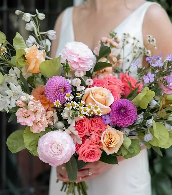 Bride holding a vibrant bouquet of pink, purple, and orange flowers against a blurred background.