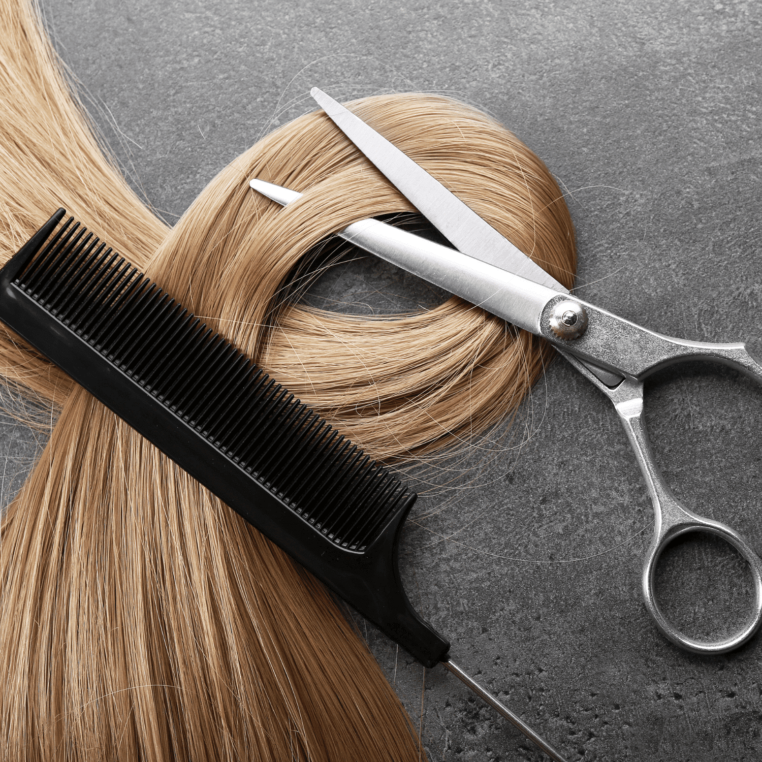 Blonde hair with scissors and comb on a dark surface, indicating a haircut setting.