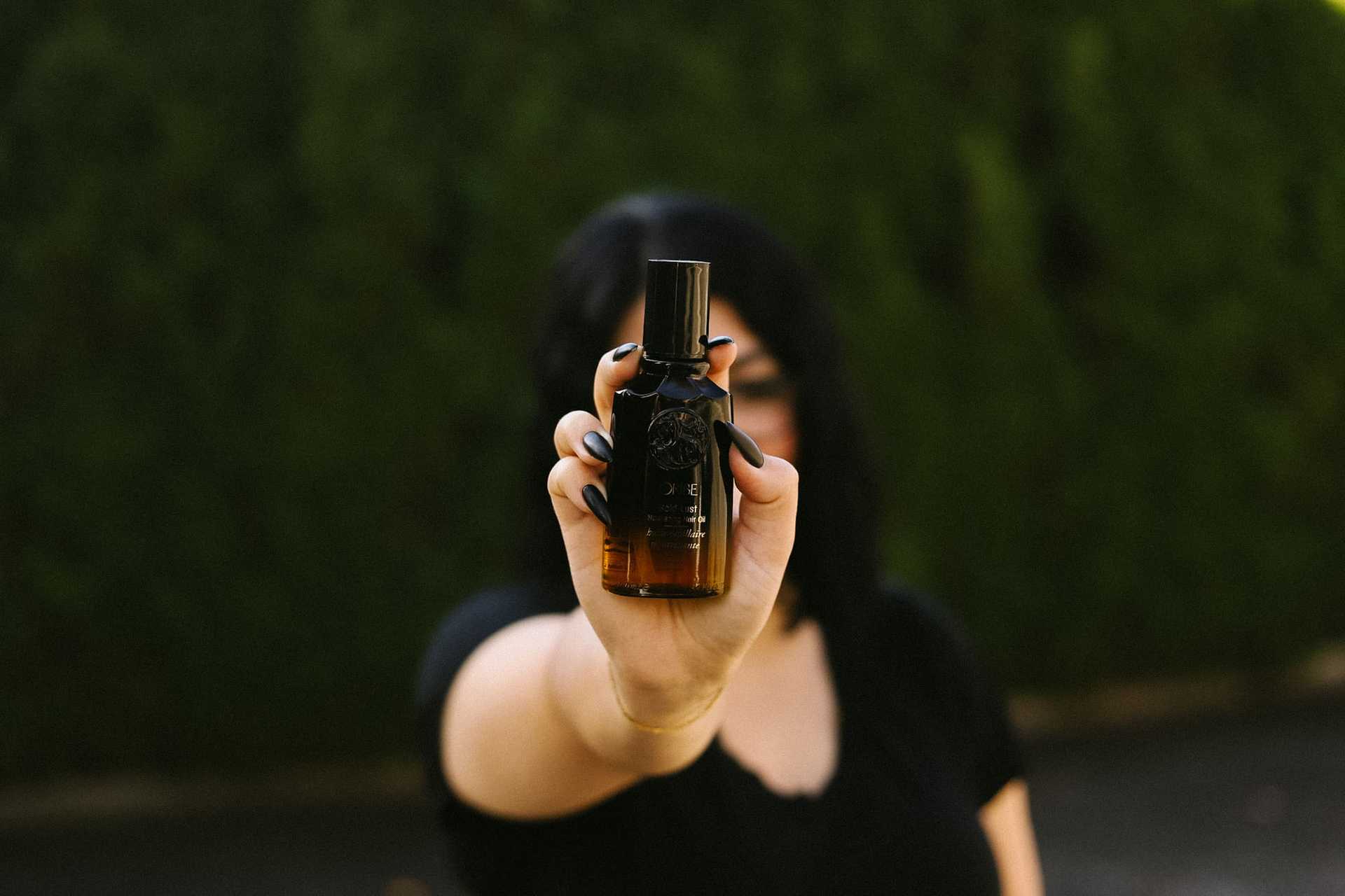A person holding a small brown bottle with a black cap, background of green foliage.