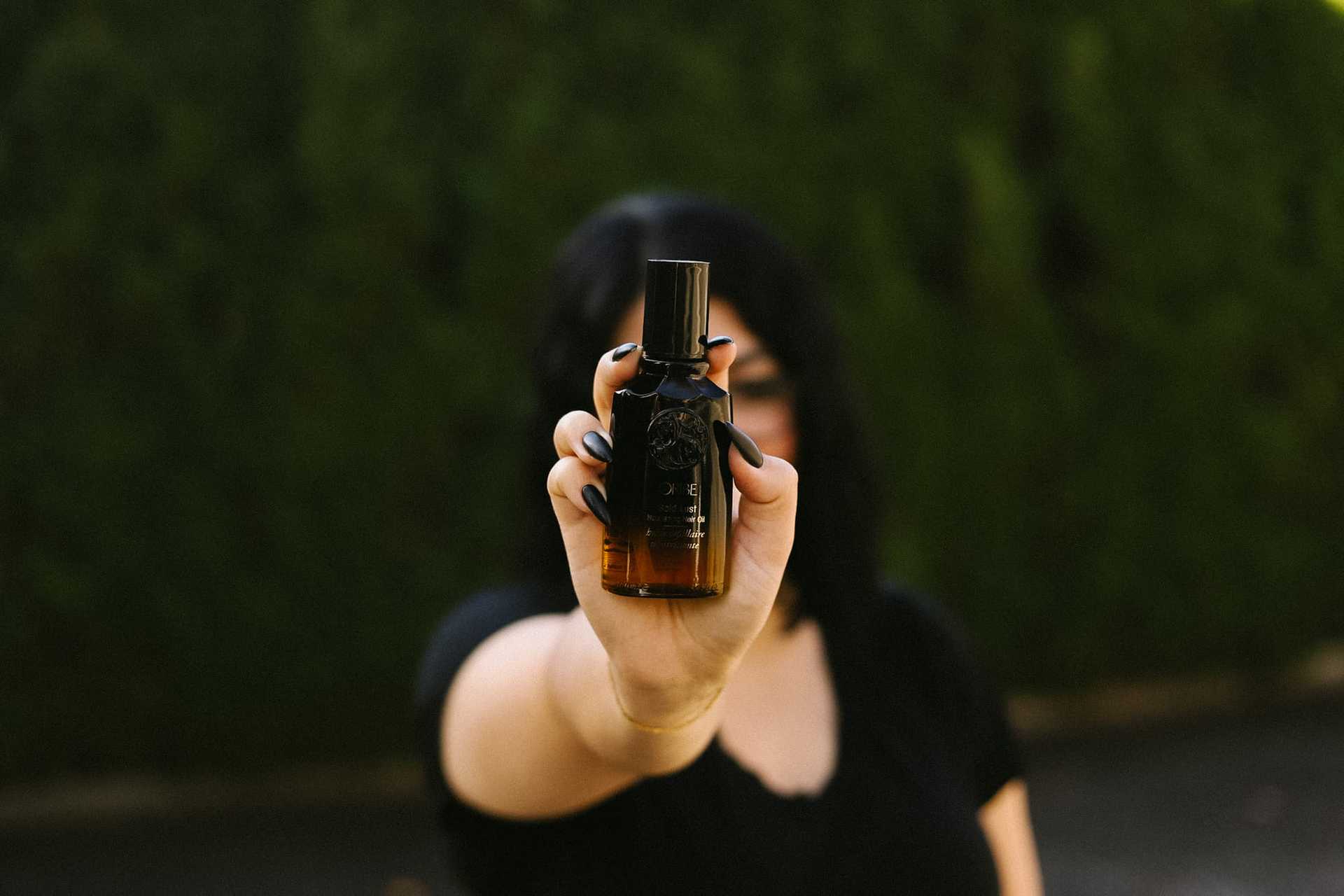 A person holding a small brown bottle with a black cap, background of green foliage.