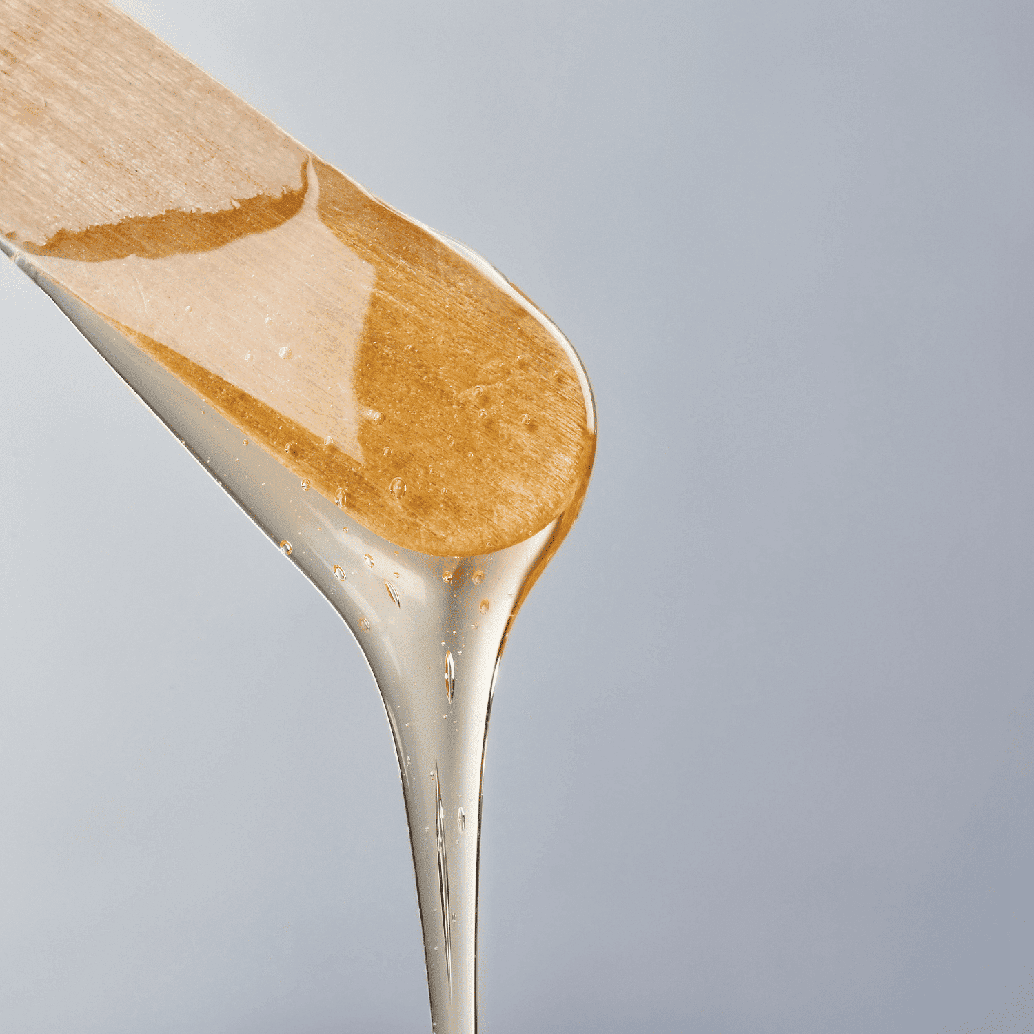 Wooden spatula with dripping golden honey against a light gray background.