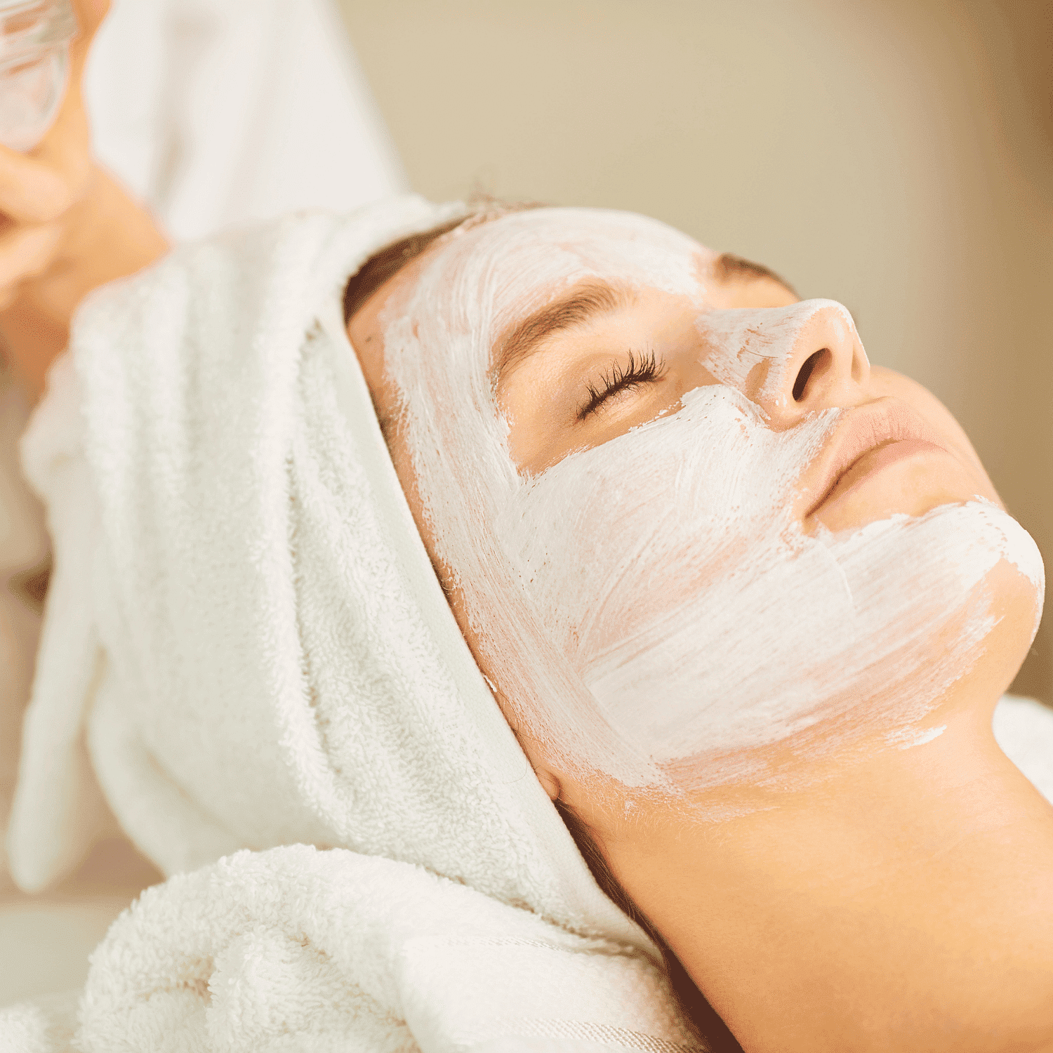 A woman receiving a relaxing facial treatment while lying with a towel around her head.