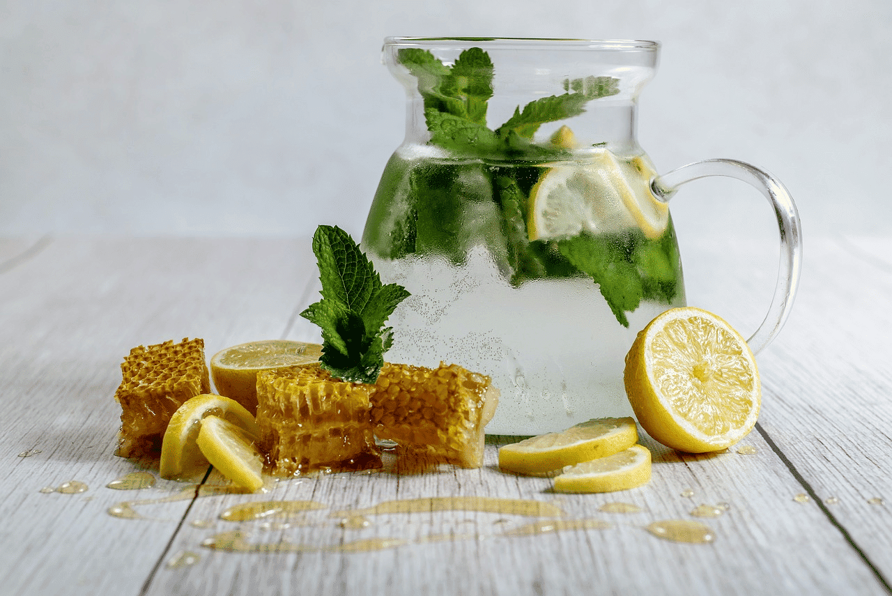 Pitcher of refreshing lemonade with mint and honeycomb on a wooden table.